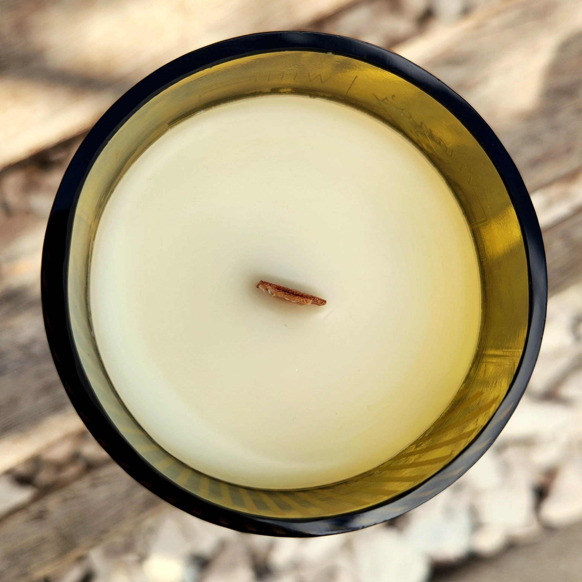 Top-down view of a clean-burning, eco-friendly candle with a wooden wick in a green-tinted recycled bottle. The creamy coconut soy wax creates a smooth surface, highlighting the sustainable craftsmanship.