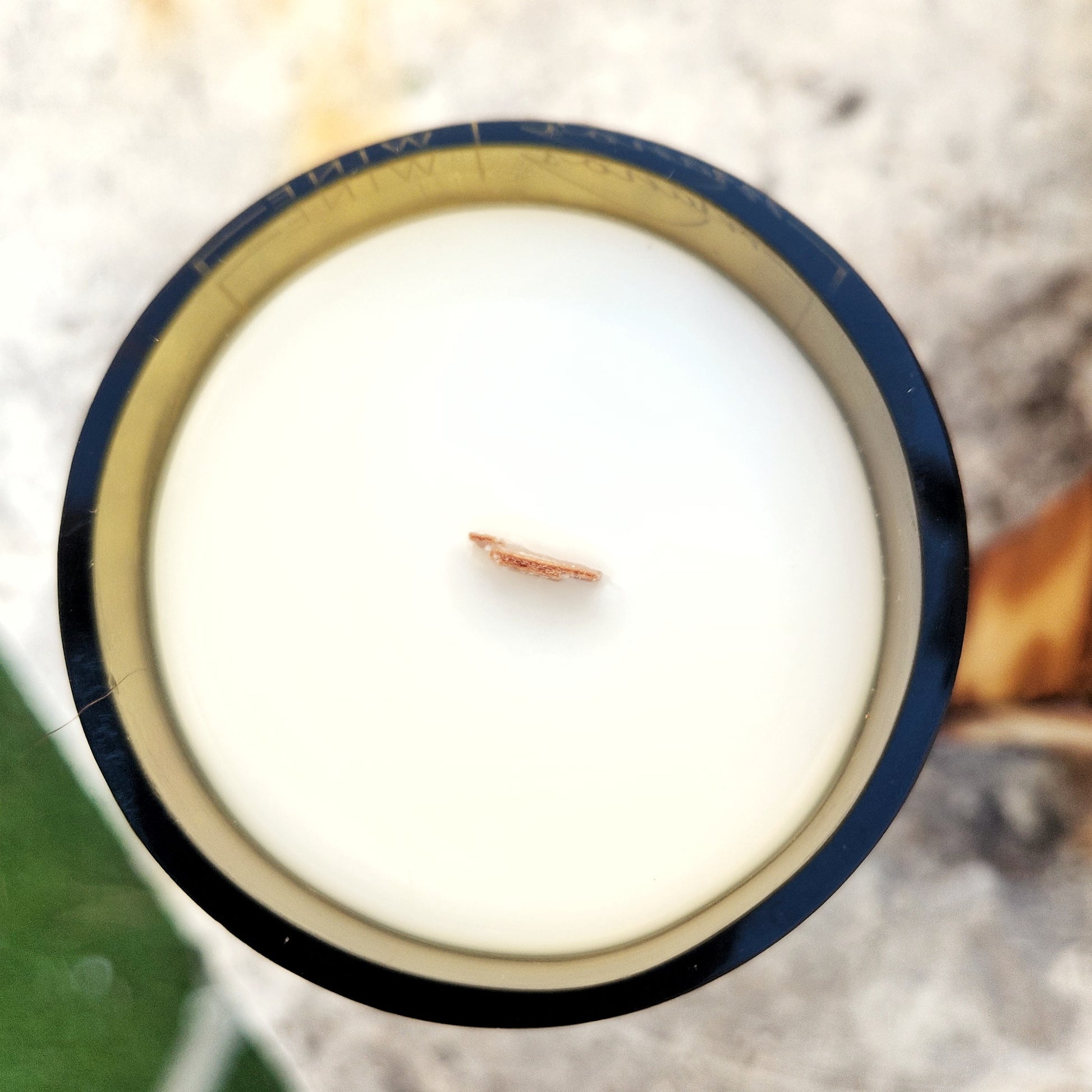Top-down view of a wooden wick candle set in a green recycled wine bottle. The white coconut soy wax fills the vessel up to the glossy, smooth rim, highlighting the candle’s clean, hand-poured finish.