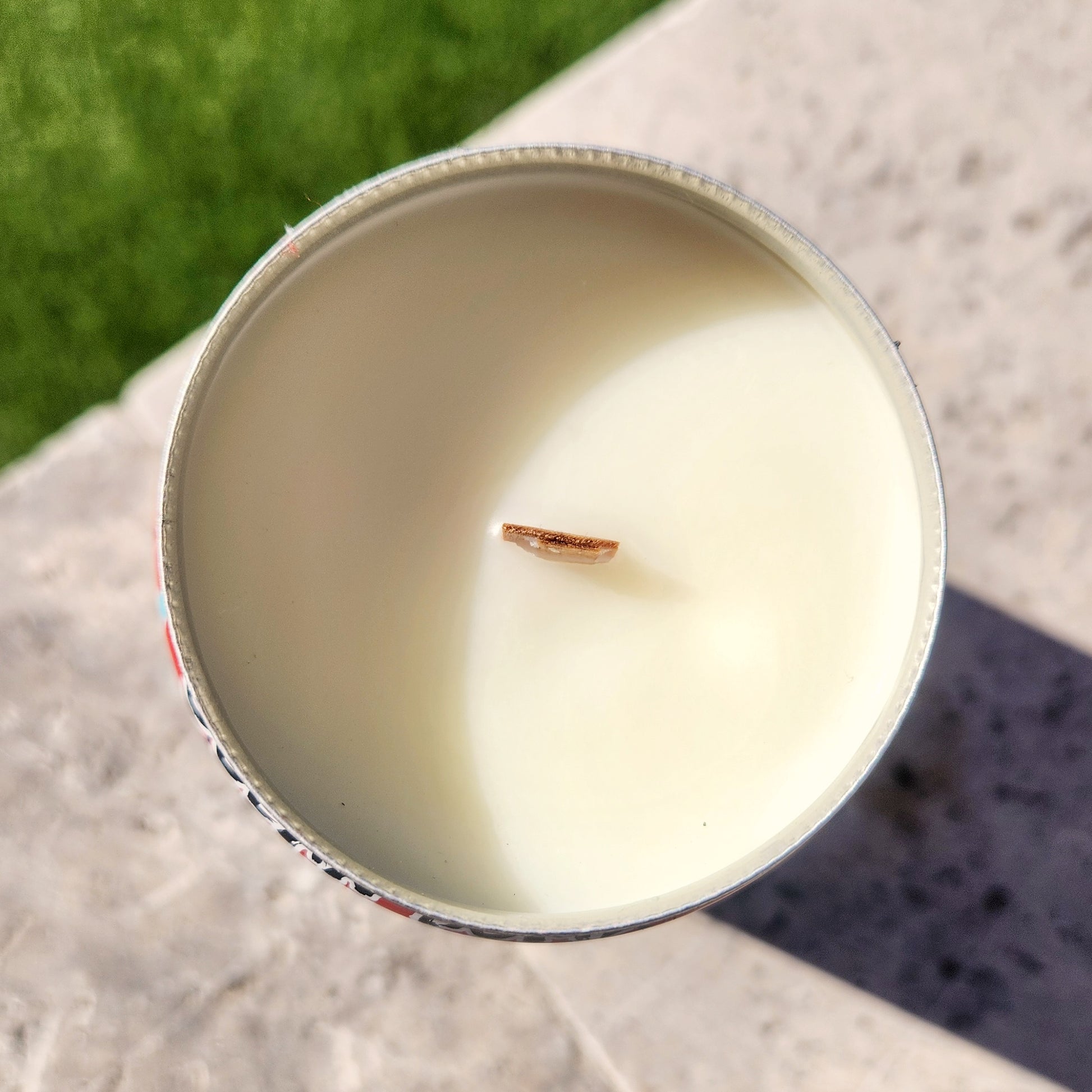 Top view of a wooden wick candle housed in a recycled red soda can, filled with creamy coconut soy wax. The eco-friendly candle has a smooth, clean surface, capturing the natural light to highlight its clean-burning qualities.