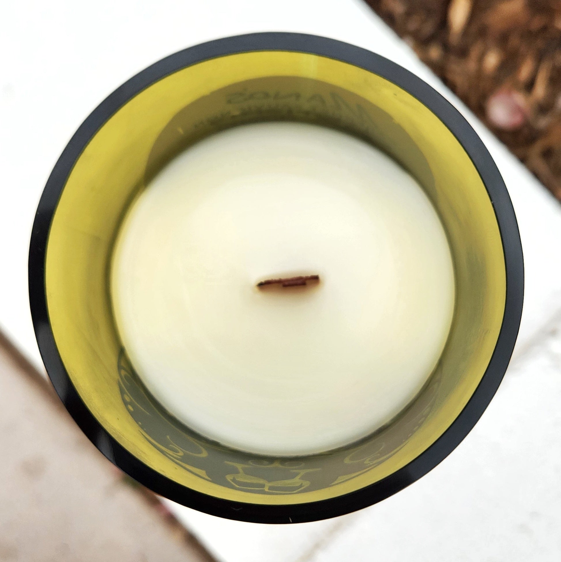 Top-down view of a hand-poured wine bottle candle featuring a smooth white coconut soy wax surface and a centered wooden wick. The upcycled green glass vessel showcases the interior imprint of a sugar skull design near the rim. This clean-burning, eco-friendly candle blends sustainability with bold style in every detail.