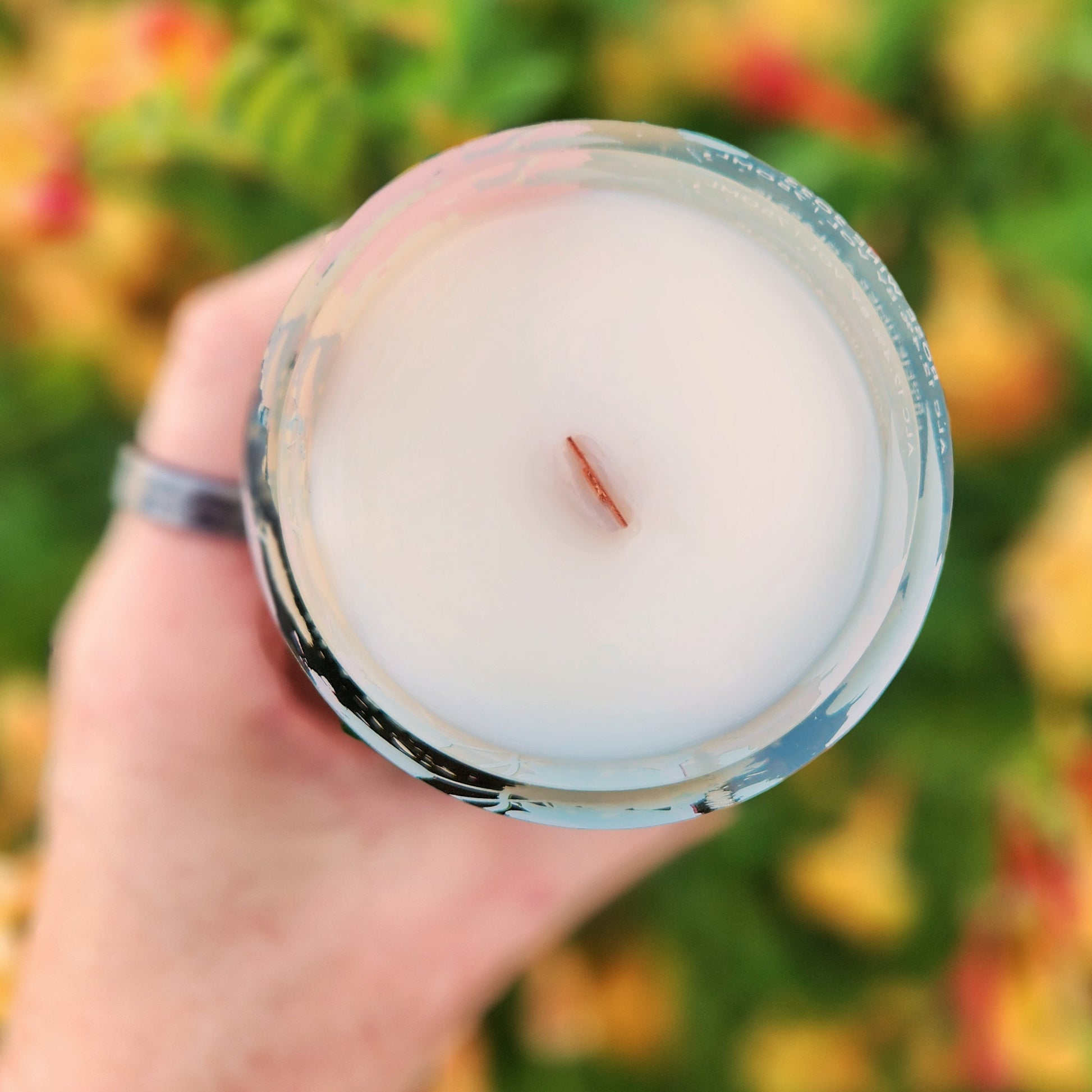 Top-down view of a handmade coconut soy wax wine bottle candle with a centered wooden wick, set in a recycled floral wine bottle. The shiny glass rim reflects the sunlight, highlighting the clean, minimalist surface and eco-friendly craftsmanship.
