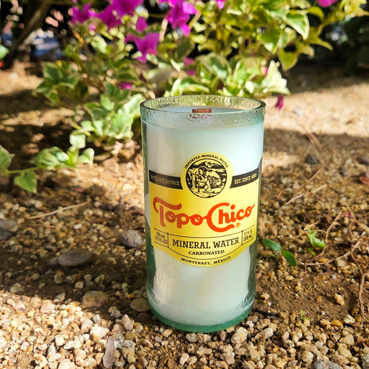 Topo Chico mineral water bottle repurposed as a candle on a gravel surface with plants in the background