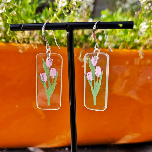 Earrings with floral design on a stand against a blurred natural background
