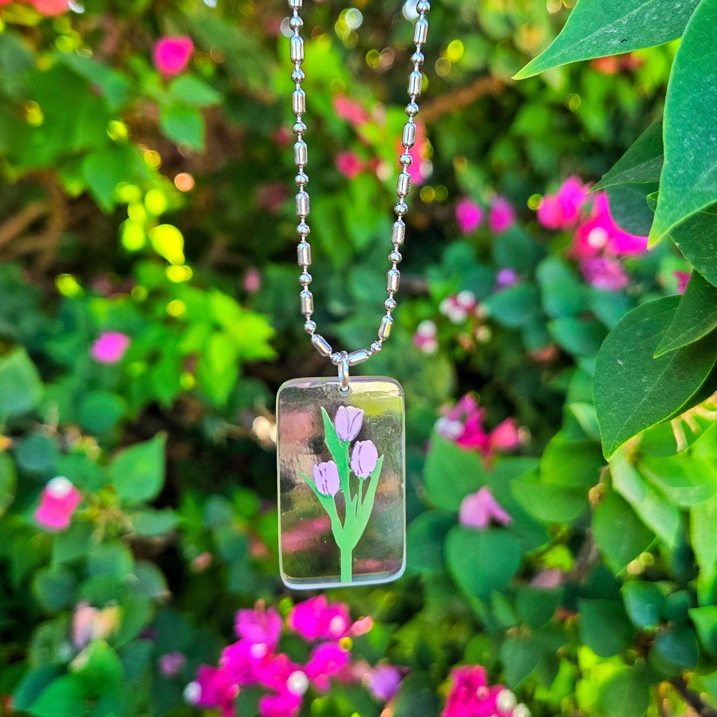 Rectangular glass pendant with floral design hanging among green leaves and pink flowers