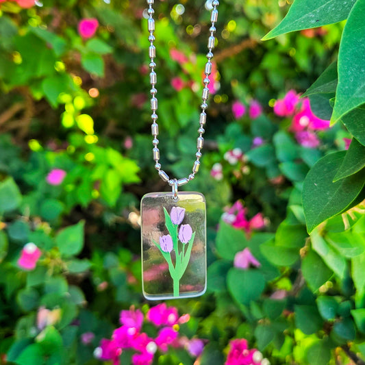 Rectangular glass pendant with floral design hanging among green leaves and pink flowers