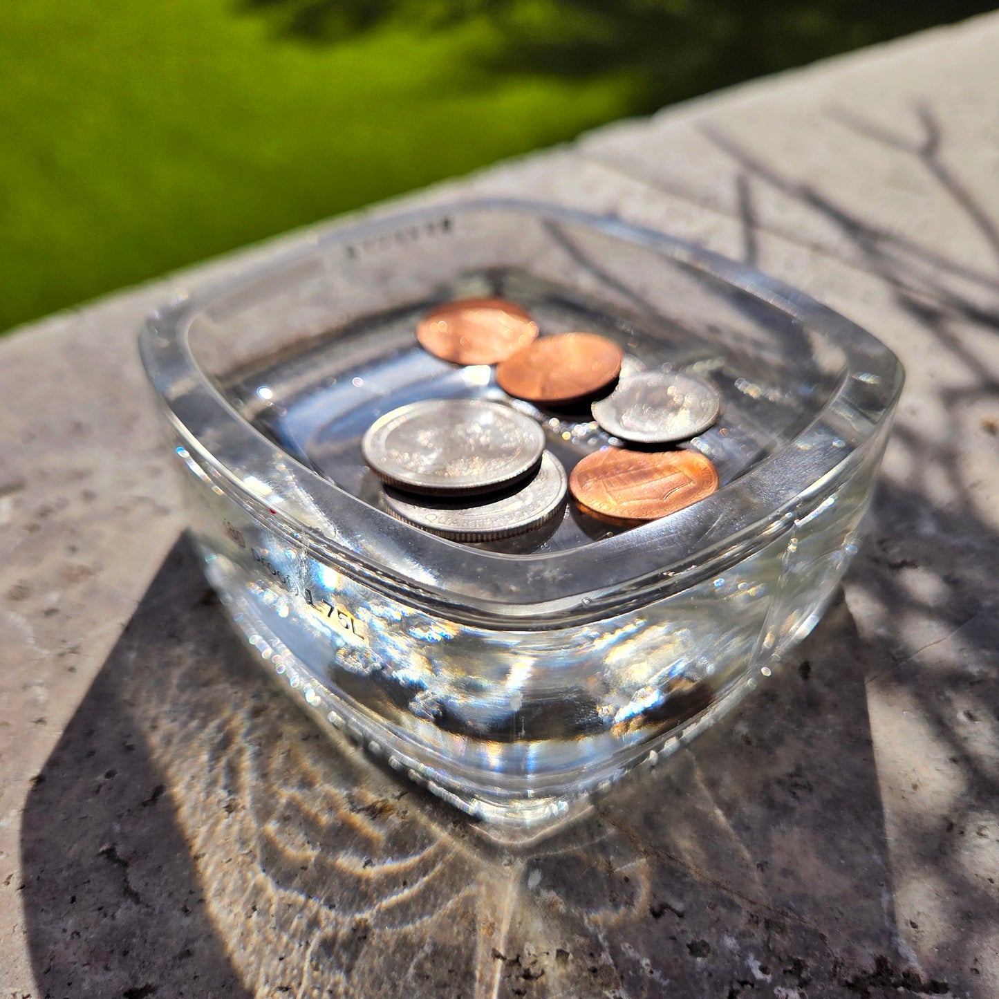 Cut clear glass tray with coins on a stone surface outdoors