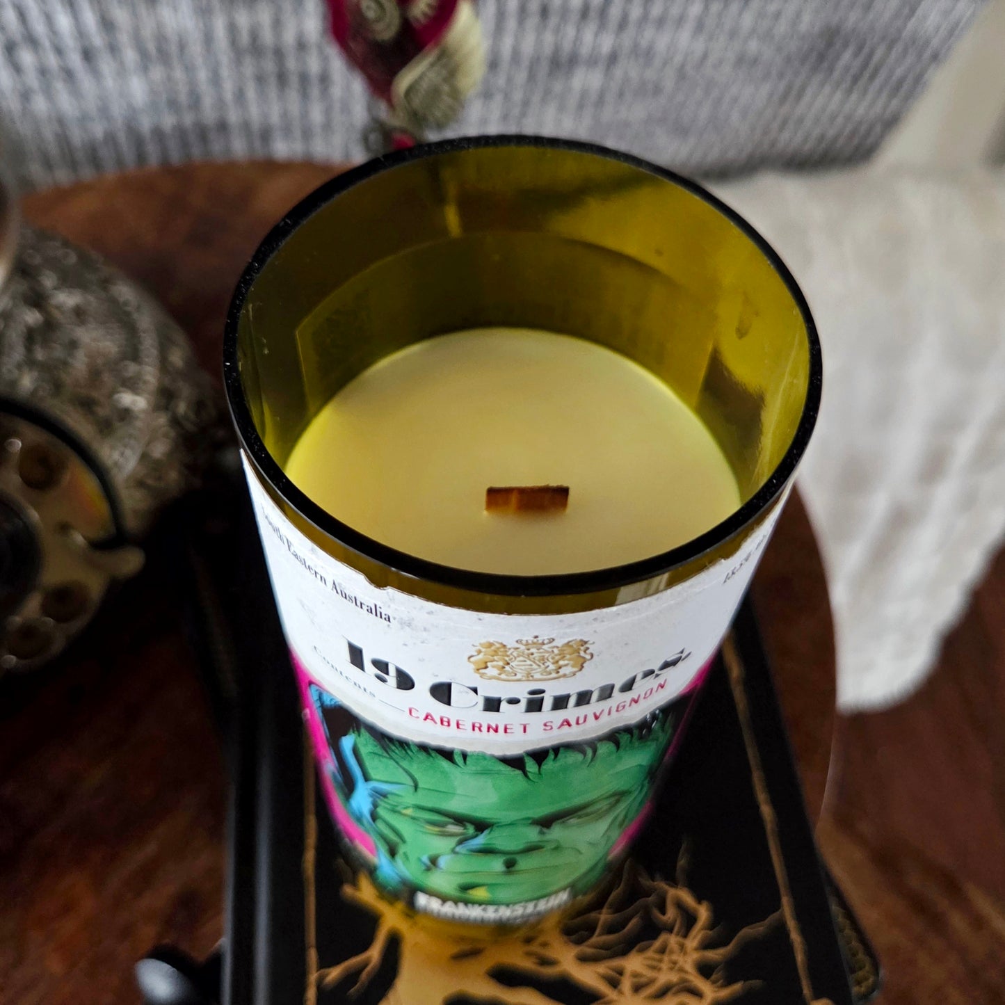 Close-up of the 19 Crimes Frankenstein wine bottle candle showing smooth coconut soy wax and a centered wooden wick inside the shiny polished rim.