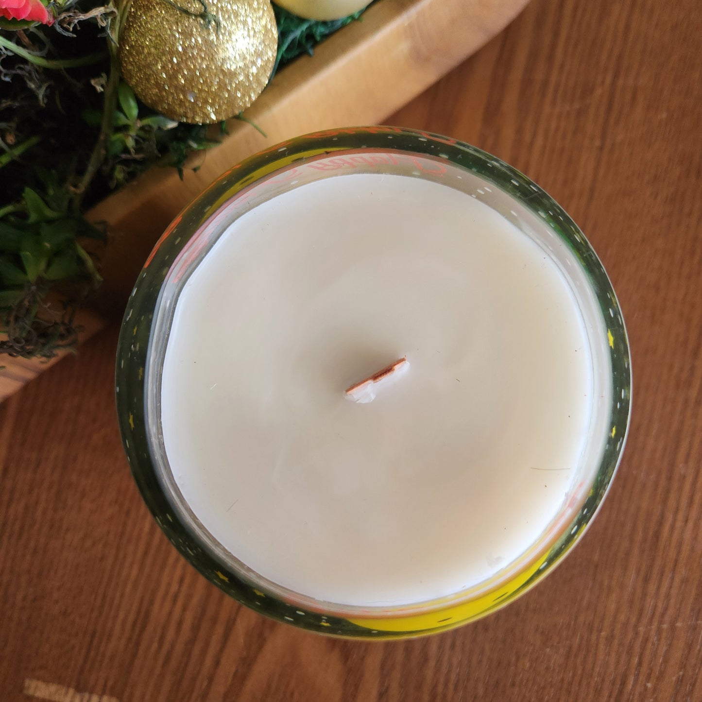 Top view of a holiday-themed wine bottle candle with creamy coconut soy wax and a centered wooden wick, set in a repurposed glass bottle adorned with Christmas graphics.