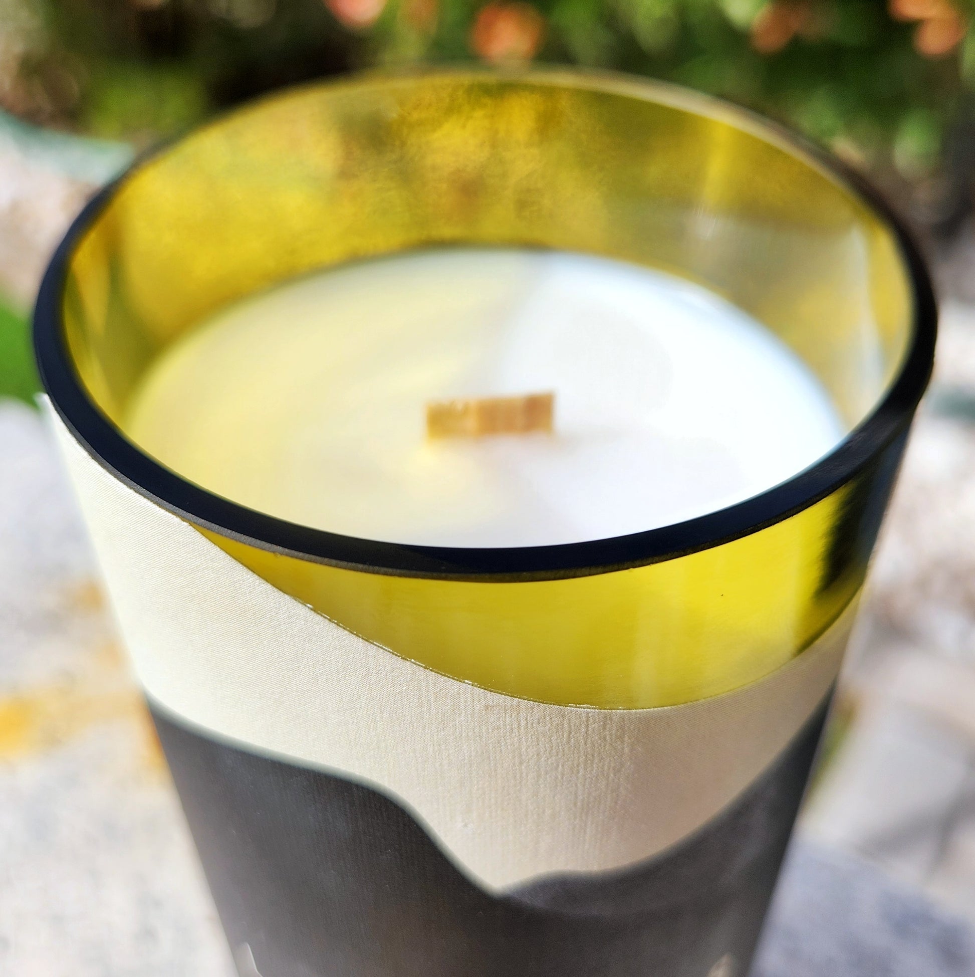 Close-up of a clean-burning coconut soy candle with a wooden wick inside a shiny smooth yellow-tinted wine bottle rim. The Los Milics label curves just below the edge.