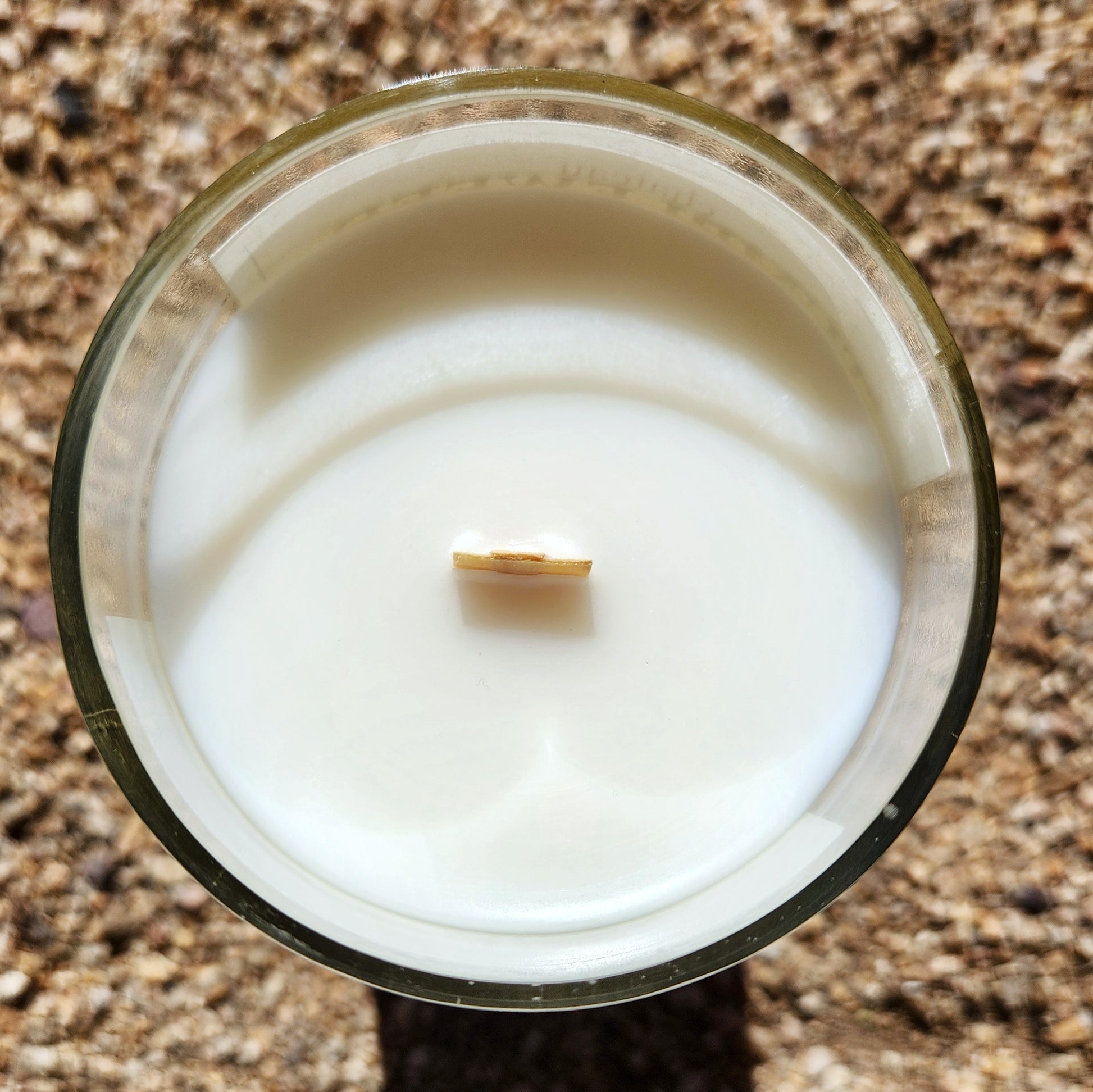 Top-down view of a hand-poured wine bottle candle made from a recycled green bottle, showcasing a centered wooden wick and creamy coconut soy wax surface.