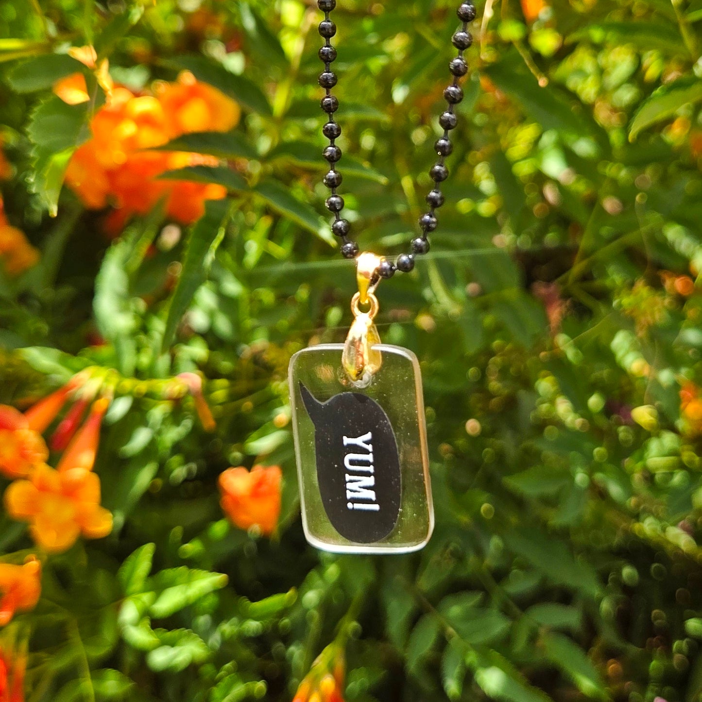 Glass milk bottle Necklace with a pendant labeled 'YUMI' against a green foliage background