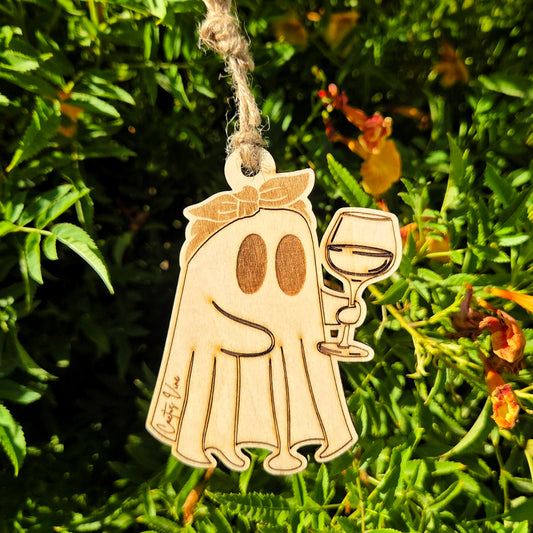 Ghost-shaped reusable wooden air freshener holding a wine glass hanging in a flowering bush