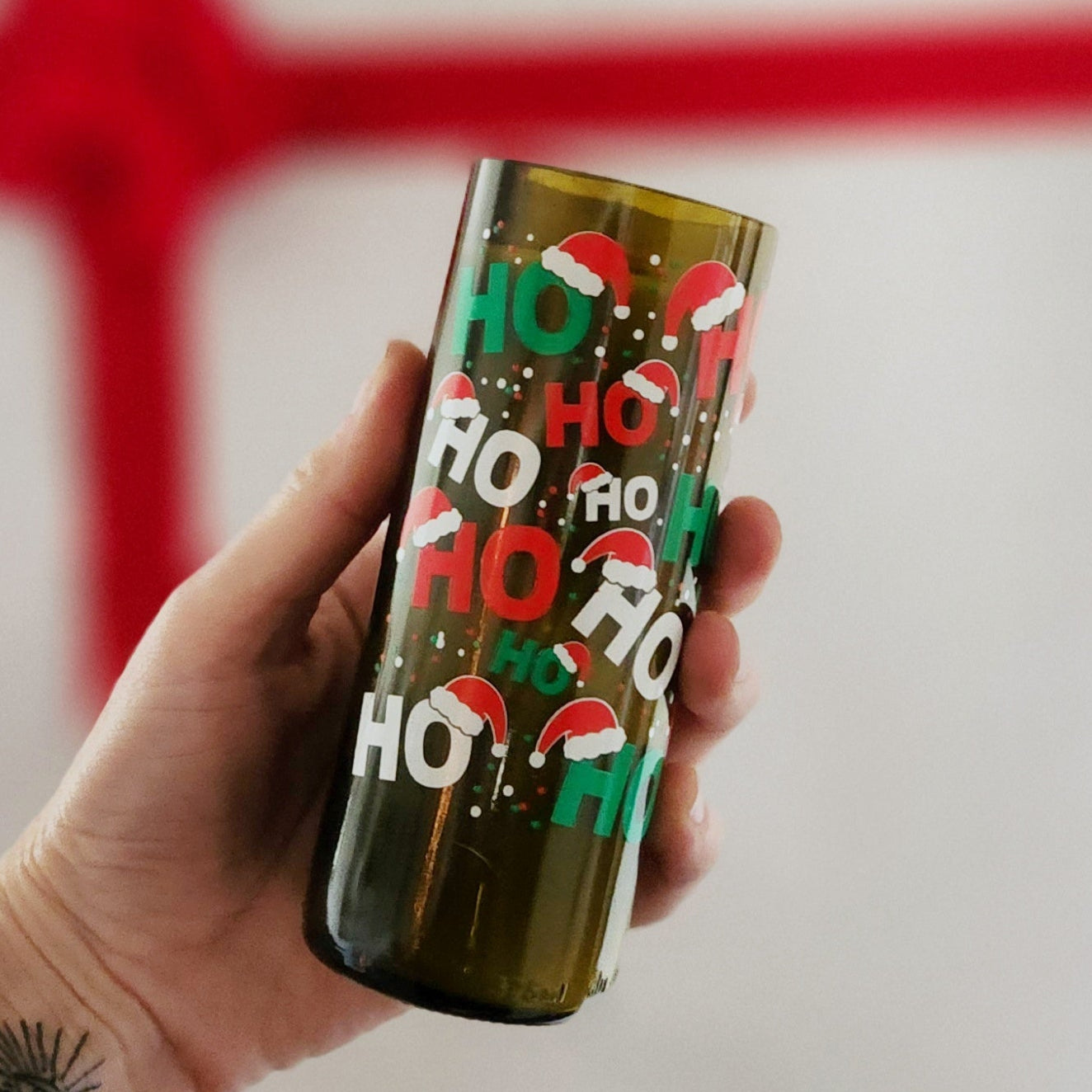 This festive candle, housed in a recycled wine bottle adorned with cheerful 'Ho Ho Ho' designs and Santa hats, brings holiday warmth to any space.