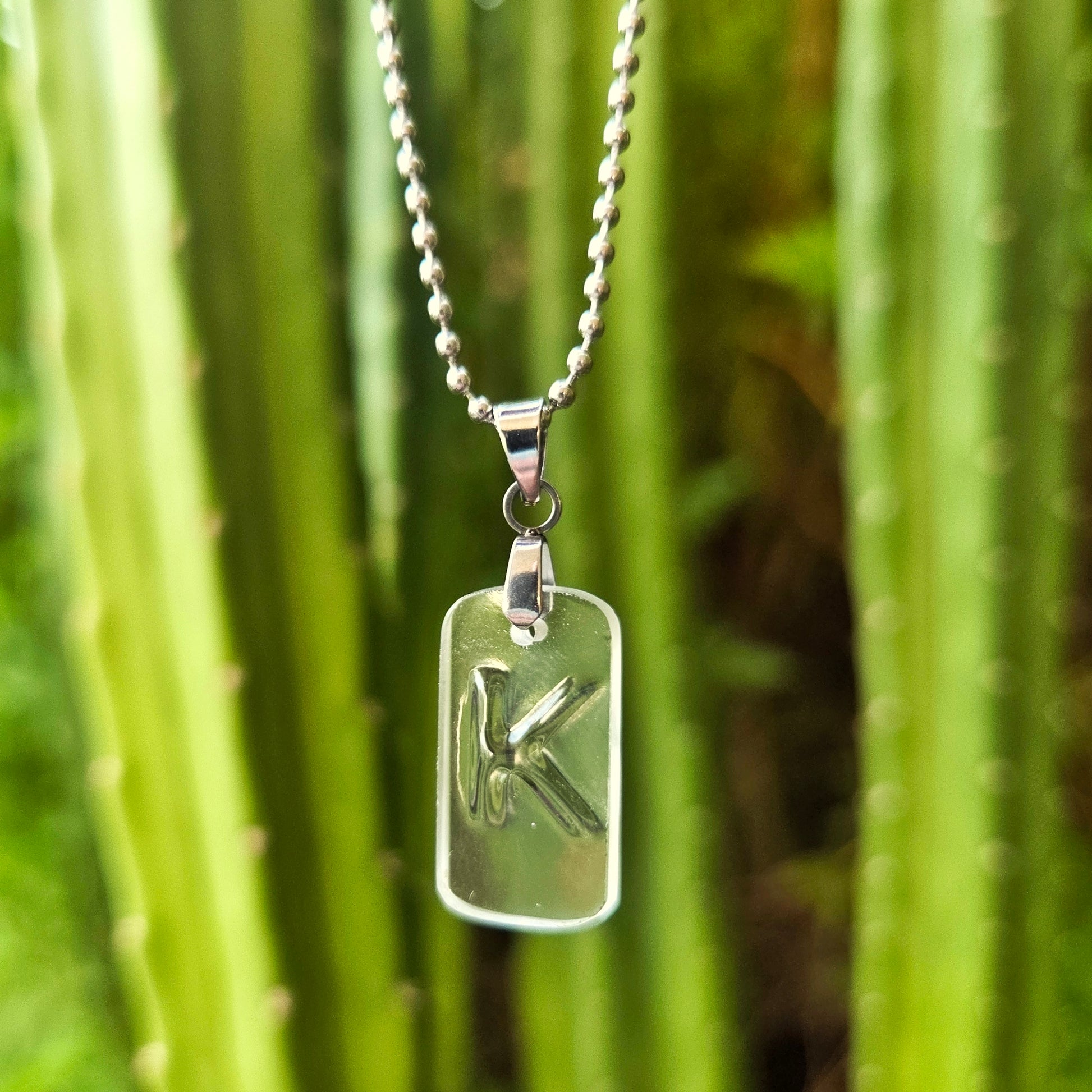 Letter K initial necklace made from clear recycled whiskey bottle glass with original raised lettering