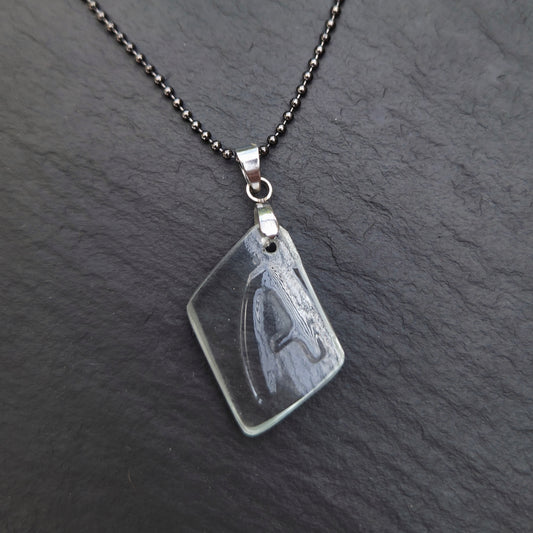 Asymmetrical clear recycled bottle glass Letter A necklace with original raised lettering, a stainless steel bail, and a gunmetal ball chain on charcoal slate.