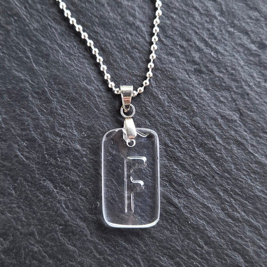 Handmade Letter F initial necklace featuring original raised lettering molded into clear recycled liquor bottle glass, with a stainless steel bail and silver-tone ball chain on charcoal slate.