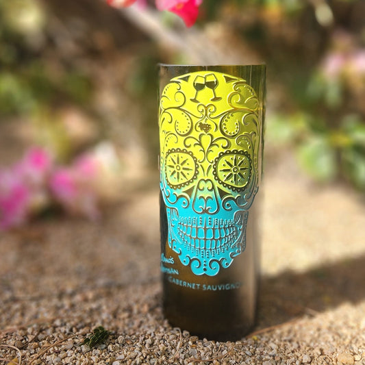 Brighten your decor with this hand-poured candle in a recycled wine bottle. Featuring a vibrant sugar skull design in neon yellow and blue, set against a floral outdoor backdrop, it’s a perfect mix of festive and sustainable charm.
