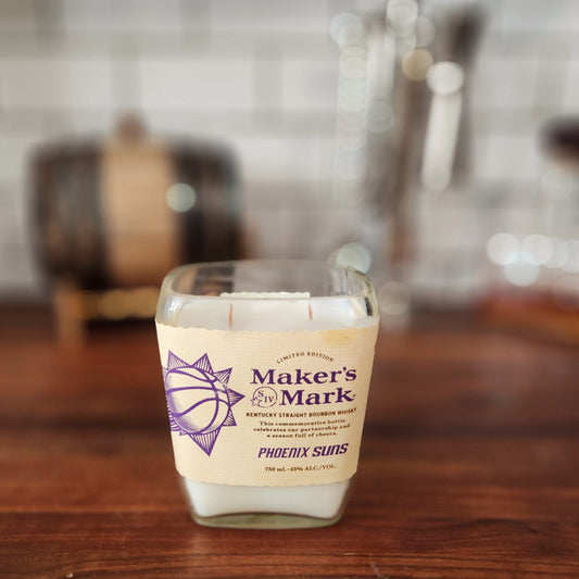 A hand-poured candle crafted from coconut-soy wax, housed in a repurposed Maker's Mark whiskey bottle with a smooth glass finish. The bottle retains its original label, featuring a limited edition design celebrating the Phoenix Suns, with purple and cream branding. The candle includes double wooden wicks for an elevated look.