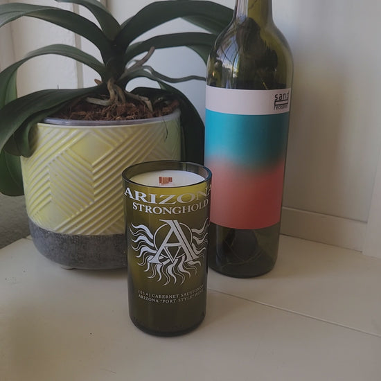 Video of Arizona Stronghold wine bottle candle being spun around, showcasing its smooth shiny rim, eco friendly wax, and wooden wick.  Plant and wine bottle in the background.