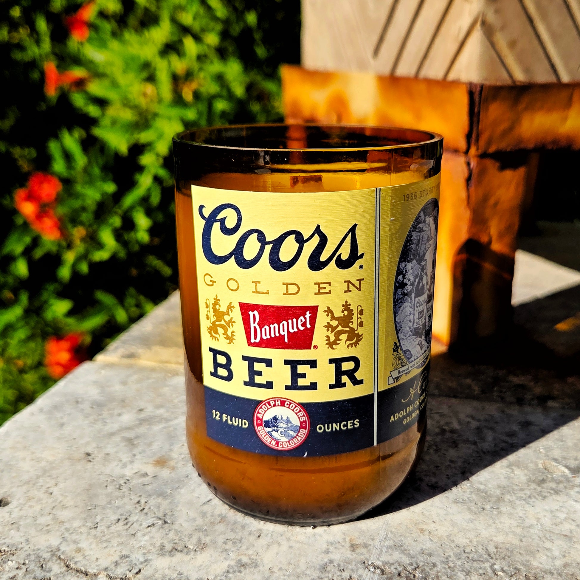 A hand-poured upcycled beer bottle candle made from a recycled Coors Banquet bottle. The 8oz candle features rich amber glass and the classic gold and navy Coors label, filled with eco-friendly coconut soy wax and a wooden wick. This clean-burning, sustainable beer bottle candle carries the Goldwater scent—a warm blend of spiced honey and vanilla—perfect for cozy, rustic home décor.
