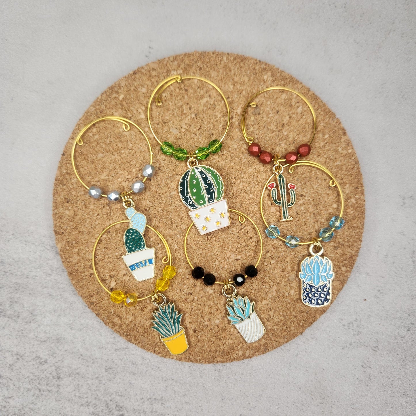 A set of cactus and succulent-themed wine glass charms arranged on a cork surface, showcasing the intricate designs and beadwork.