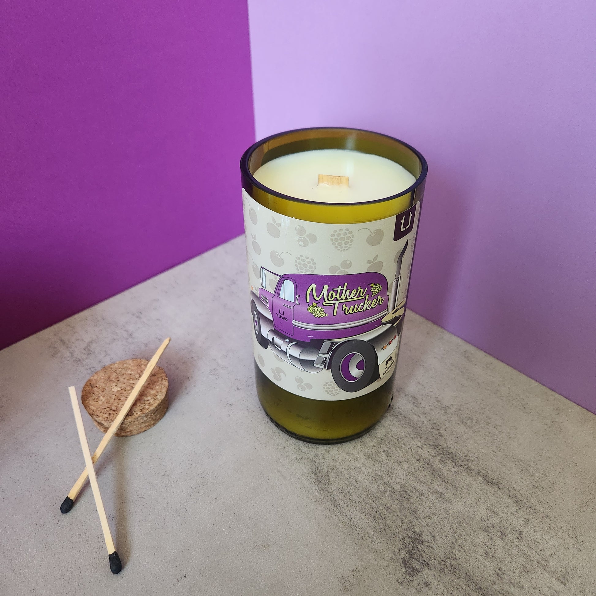 Sage & Lavender scented candle in a recycled wine bottle, displayed on a concrete surface with purple background and matches placed beside it.