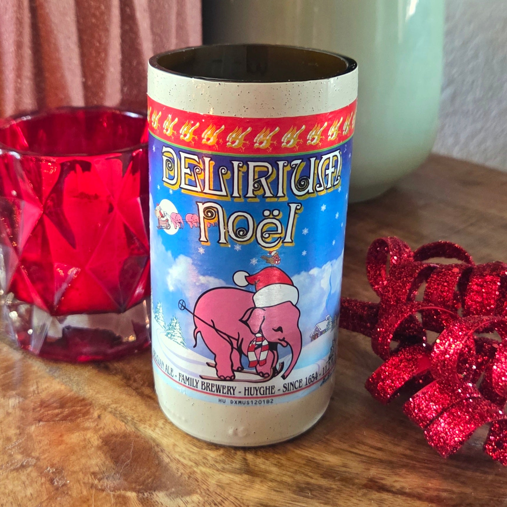 Delirium Noel beer can with festive design on a wooden surface with red glass and bow.