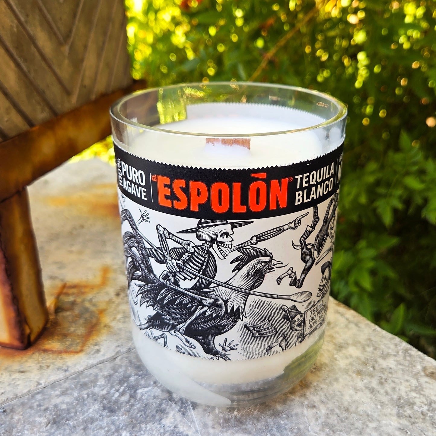Glass with Espolón Tequila Blanco label on a stone surface with greenery in the background